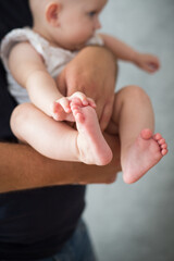 Rodzice trzymają w rękach swoje malutkie dziecko, stopy i rączki dziecka w dłoniach rodziców - obrazy, fototapety, plakaty