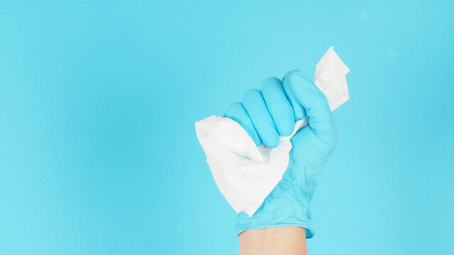 Hand wear medical glove and hold crumple tissue paper on blue background . Studio picture.