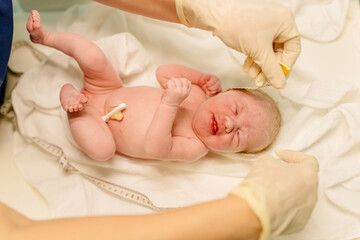 Newborn baby being examined by midwife moments after birth with tape measure and gloves checking...