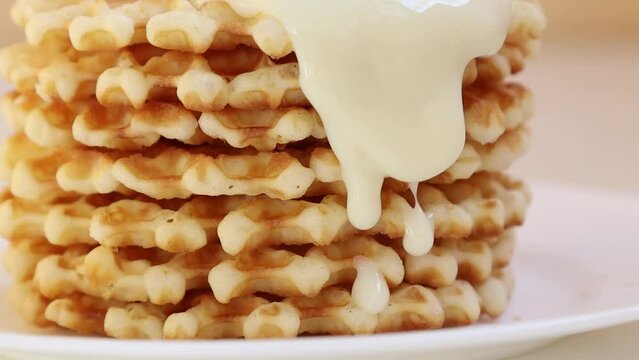 Delicious dessert a stack of waffles on a plate poured with condensed milk, which flows and drips onto the plate