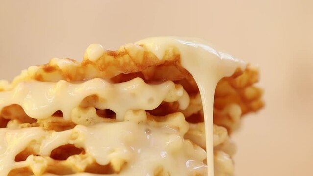 Condensed milk thickly and a lot flowing in large drops and streams over a cake of delicious homemade waffles snack or dessert