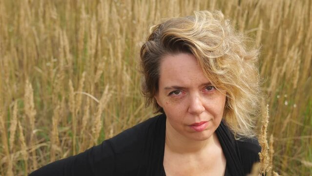 Portrait of a forty-year-old blonde woman in black clothes near dry grass. Slow motion portrait. Relax in nature.