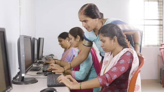 smiling teacher and student looking at camera while teaching computer class to woman's at village - concept of volunteer, self employment training and empowerment programs