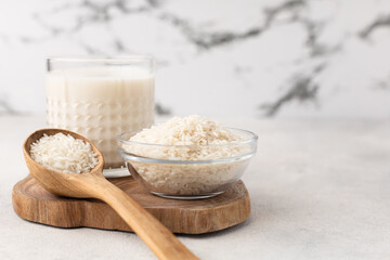 Glass cup of rice milk with a bowl of rice on a light background