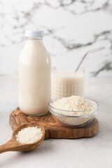 A bottle and a glass of rice milk with a bowl of rice and a wooden spoon on a wooden board on a...