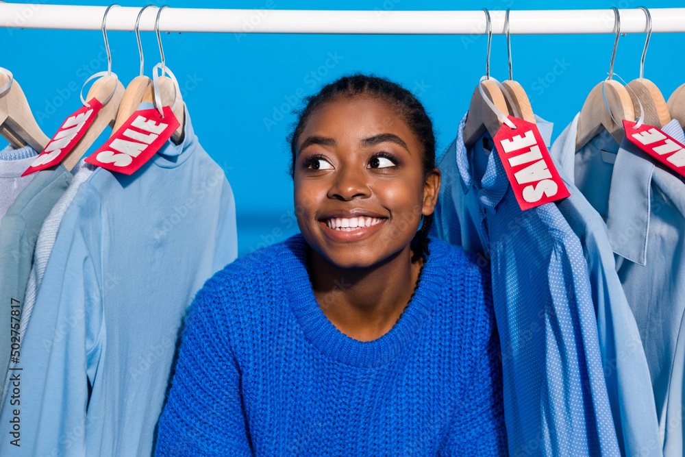 Wall mural Portrait of attractive cheerful girly girl customer choosing new wear look shirt isolated over bright blue color background