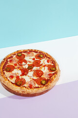 Italian pizza with ham, pepperoni and jalapeno on coloured background. Meat pizza with salami and chilli pepper in minimal style on blue color. American pizza delivery concept with color backdrop