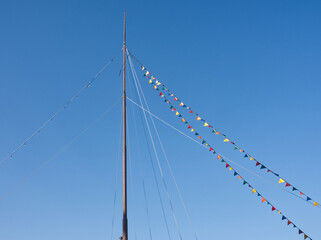 Boat mast draped in colorful flags and pennants on blue sky background. Triangle flag and bunting on ship or yacht lines. Travel and vacation layout, copy space for text. Sea, nautical greetings card.