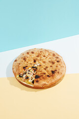 Italian closed pizza with mushrooms, potatoes and chicken on coloured background. Mushroom pie with cheese and chicken in minimal style. American pizza delivery concept with color backdrop.