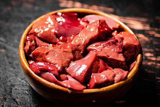 The wooden bowl on the table is full of sliced raw liver. Against a dark background. High quality photo