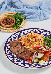 Traditional uzbek food - plov with beef. Eastern cuisine - pilaf with rice, meat and spices. Plov with beef on traditional uzbek plate. Composition of oriental ceramic plate with pilaf.