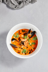 Traditional asian food - tom yam kung with prawn and mussels. Tom yum soup with seafood and coconut milk. Tom yam in ceramic bowl on gray stone background. Oriental cuisine. Asian menu.