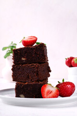 Stack of pieces of chocolate brownie with nuts and strawberry on the white plate. Homemade dessert