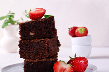 Stack of pieces of chocolate brownie with nuts and strawberry on the white plate. Homemade dessert
