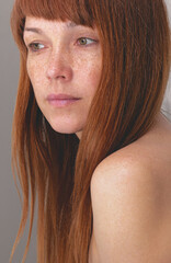 Portrait of caucasian middle-aged woman with reddish hair and freckles looking aside over gray...