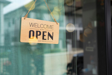 Open and closed flip sign in front of coffee shop and restaurant glass door. Wooden sign with wording of place's status. Say Welcome.