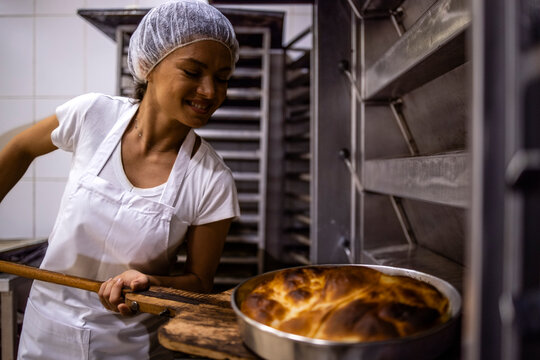 Female baker taking out freshly baked pie from the oven in bakery food production.