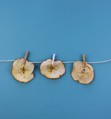 Dried apples hang on clothespins on a blue background. Drying fruits at home