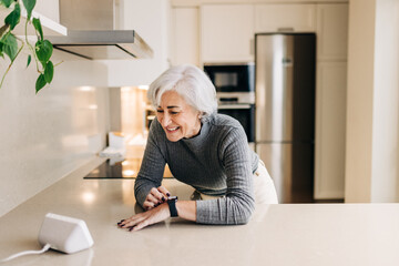 Senior woman using smart devices in her kitchen at home - obrazy, fototapety, plakaty