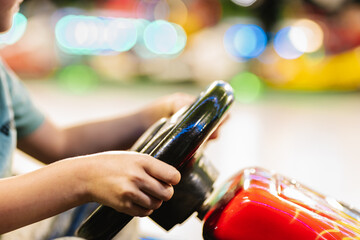 Hands of a child holding the steering wheel of a car at the amusement park.