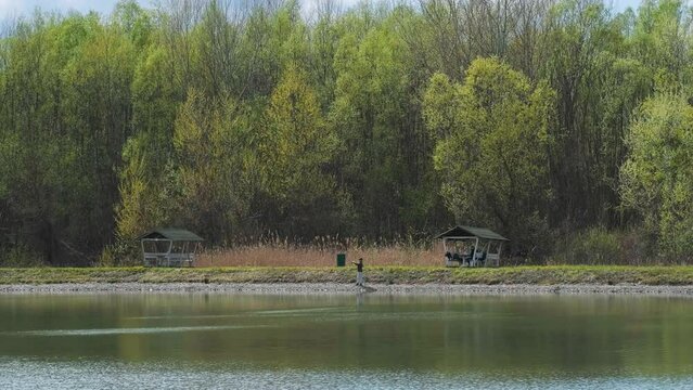 Fisherman, lake, forest. Fisherman in his hand holding spinning. Fishing, spinning reel, fish, Breg rivers, fishing. Fisherman standing on the shore of lake with fishing rod. Man fishing on a lake