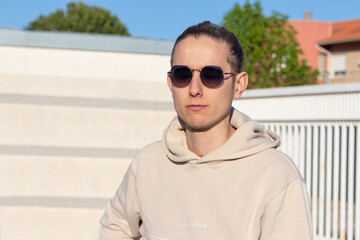 Portrait of a young man in a beige sweatshirt and black sunglasses on a spring day looking to the sun