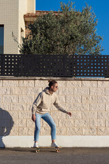 Vertical view of young skater man with bun hairstyle on Street Against white brick Wall wjearing a sweatshirt and jeans