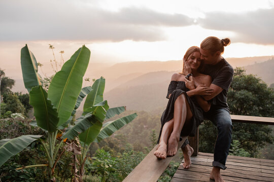 A couple in love sits and hugs on a balcony overlooking the sunset in the mountains