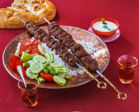 Grilled Adana kebab skewers on a plate with rice and salad
