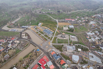 Fototapeta premium Ancient stone bridge across Kars River & Kars Castle - main tourist attractions of Kars, Turkey. Near flag (on castle) are portrait of Ataturk & writing in Turkish 'Motherland remembers you'