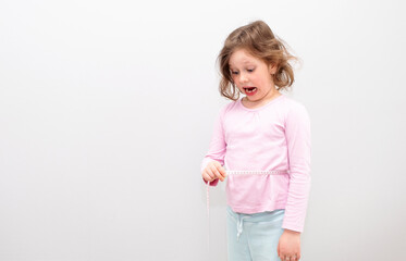 Caucasian girl 6 years old, in a yellow sweatshirt with a hood on a gray background. The child poses for the camera, measures his waist and is surprised.