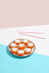 Philadelphia maki roll on ceramic plate with chopsticks. Salmon sushi roll with philadelphia cheese on coloured background. Japanese menu concept. Salmon sushi roll in modern style.