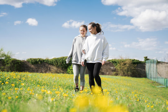 Woman Walking With Her Teen Daughter Through The Field With Flowers During The Summer Day