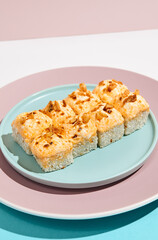 Baked Maki roll with chicken and cheese on ceramic plate. Hot sushi roll with cheese topped and crispy onion on coloured background. Japanese menu concept. Hot sushi roll in modern style.
