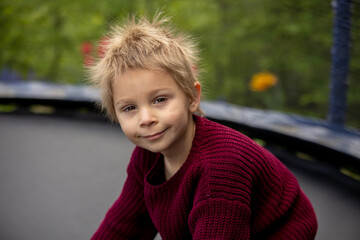 Cute little boy with static electricy hair, having his funny portrait taken outdoors on  trampoline