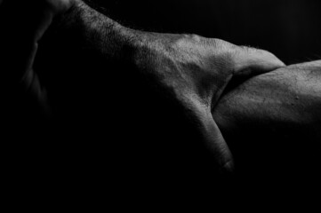 Close-up view in black and white of two hands holding each other's wrist, sign of help and support, on black background