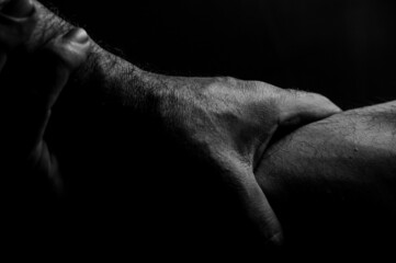 Close-up view in black and white of two hands holding each other's wrist, sign of help and support, on black background