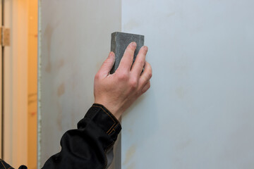 Worker sanding the drywall mud using sand trowel during renovation the house on room