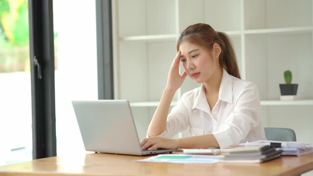 A young businesswoman is looking stressed as she works at her computer, Asian woman got headache from working on notebook all day long.