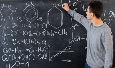 the teacher writes on the blackboard various formulas for chemistry in high school. young Arab teacher.