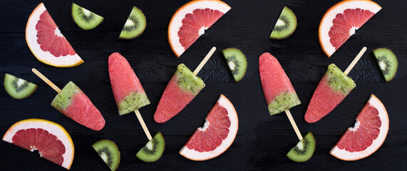Top view of popsicle stick with kiwi and grapefruit on the black wooden  background. Closeup.