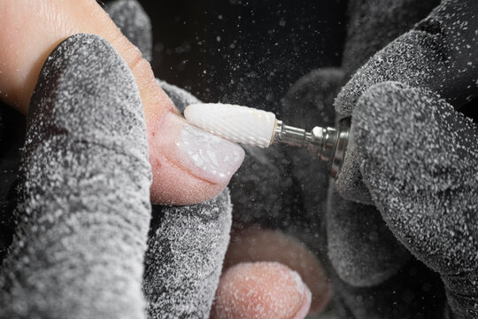 Closeup shot of master in rubber gloves applying an electric nail file drill to remove the nail polish in the beauty salon. Perfect nails manicure process with flying dust or debris