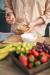Woman adding muesli into the bowl with yogurt