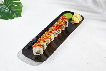 Maki sushi with salmon and teriyaki sauce on black plate. Maki roll with salmon tartare outside and tuna, cheese and cucumber inside. Sushi menu on white background with hard shadow and leaves.