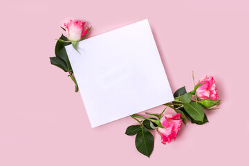 Invitation or greeting card mockup with a blank sheet and some delicate pink roses on a pastel pink background.