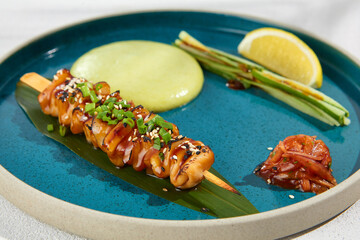 Squid yakitori in ceramic dish on white background. Japanese skewered squid with wasabi sauce. Grilled kalmar on bamboo skewer in asian style. Food menu for izakaya. Summer pan asian menu. © Ryzhkov