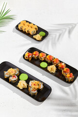 Set from tempura sushi in black plate on white background. Hot maki sushi with wasabi and ginger. Sushi menu with shadows and tropical leaves.