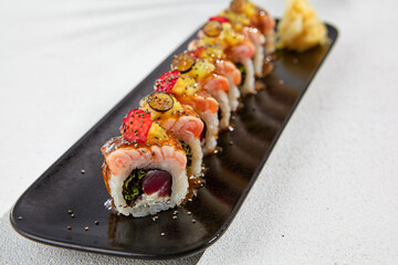 Modern asian food - maki sushi with salmon and berries on black plate on white concrete background....