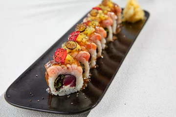 Fotobehang Modern asian food - maki sushi with salmon and berries on black plate on white concrete background. Sushi roll with tuna inside and salmon, mango and berries outside. Fusion sushi menu. © Ryzhkov