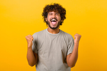 Overjoyed crazy happy Indian curly guy screaming yes in ecstatic, raising fists up, celebrating...